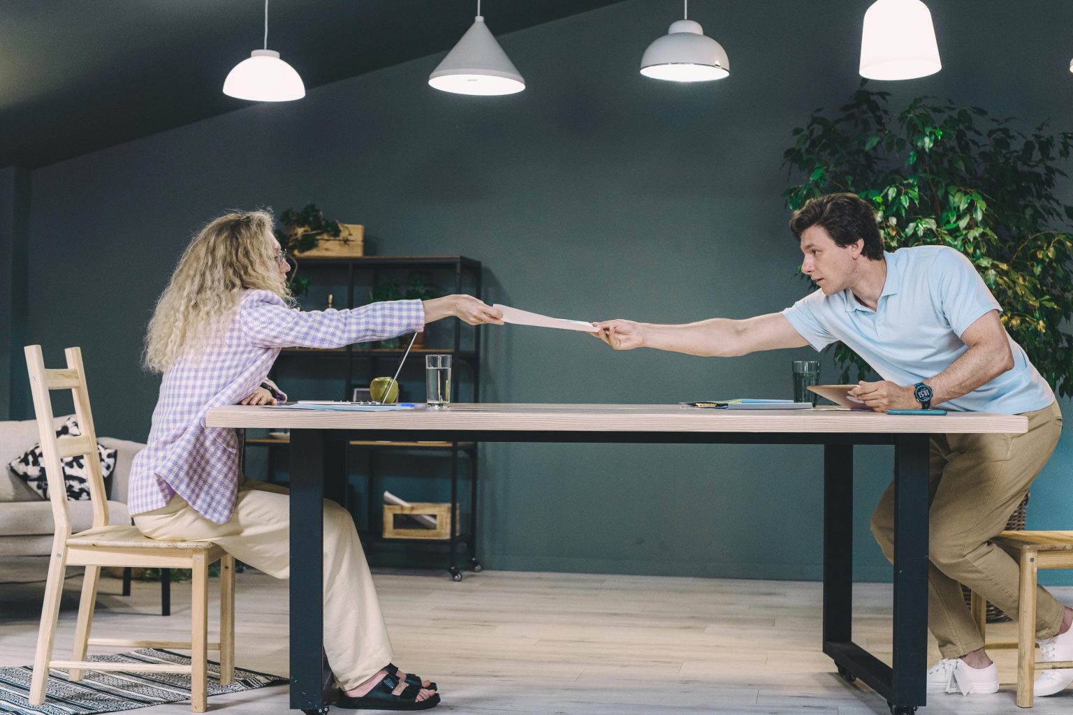 man en vrouw geven een document door over tafel, illustratie bij een blog over waardeoverdracht nu doen of nog even wachten