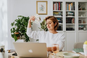 Vrouw achter laptop met geld in hand bij lijfrente en sparen